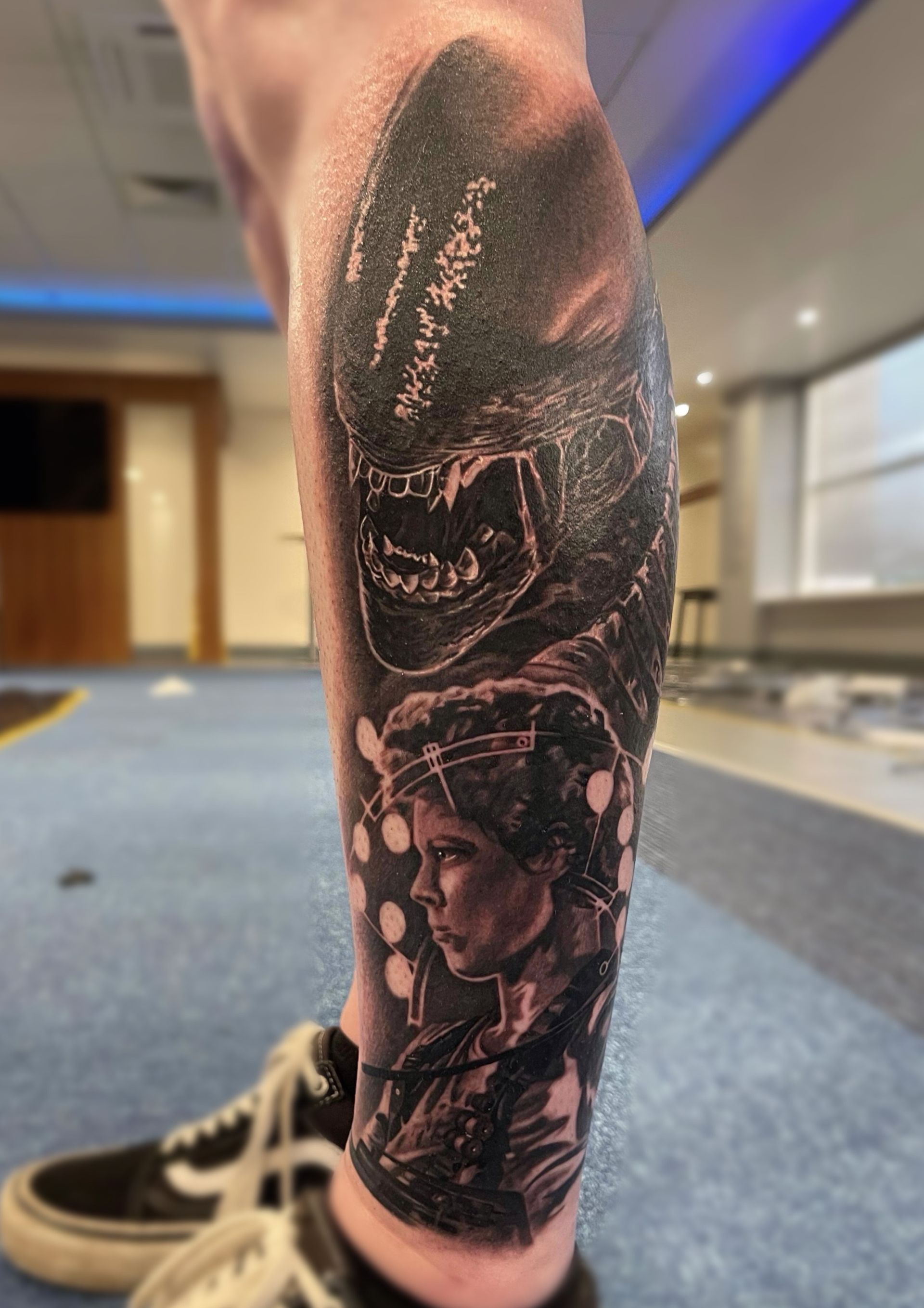A person has a tattoo on their leg of a monster and a woman.